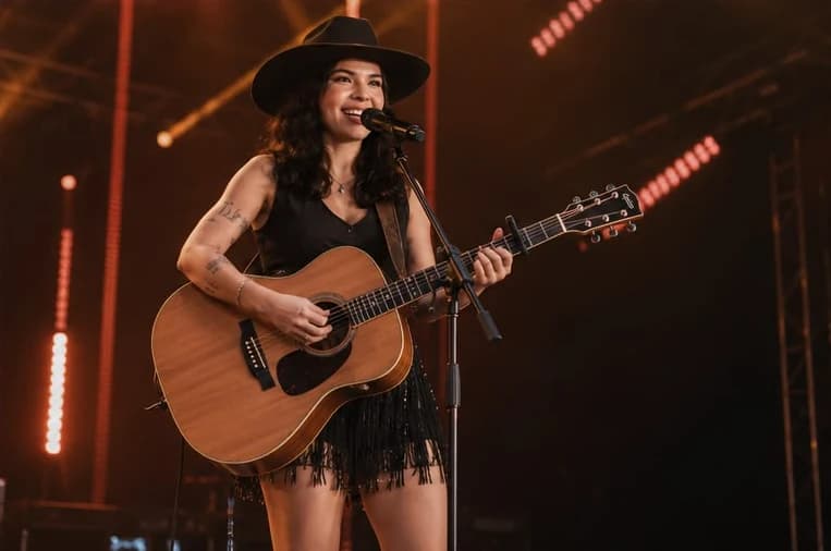 Layra Mota com violão em palco de luzes quentes