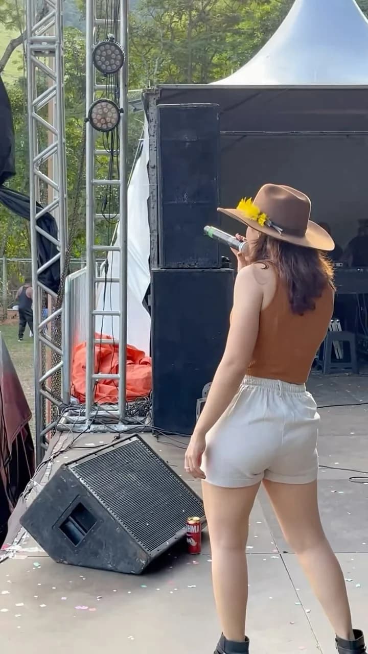 Layra Mota cantando em festival, de chapéu com girassóis